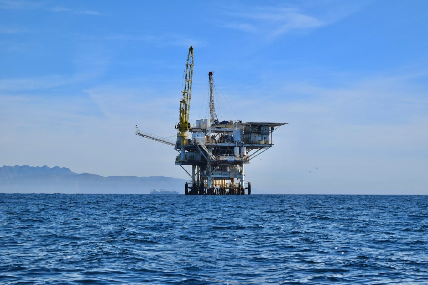 Offshore oil rig with cranes in a blue sky over calm sea waters.