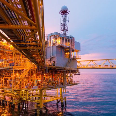 Oil rig platform at sunset, with communications tower and vibrant orange lights.