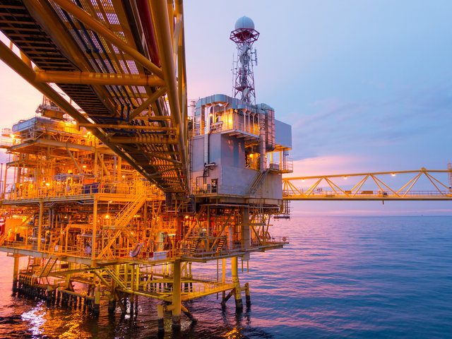 Offshore oil rig at sunset, illuminated against the sea and sky.