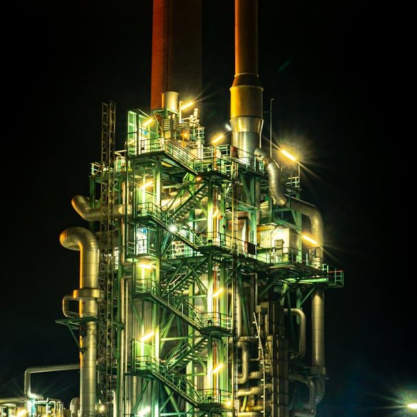 Night view of a brightly lit industrial facility with tall chimneys.