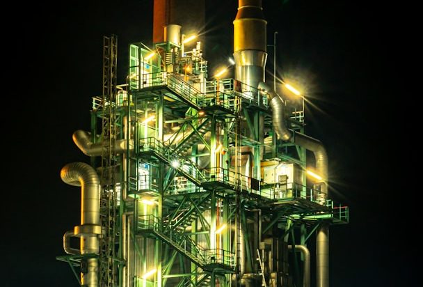 Illuminated industrial structure with pipes and machinery at night.