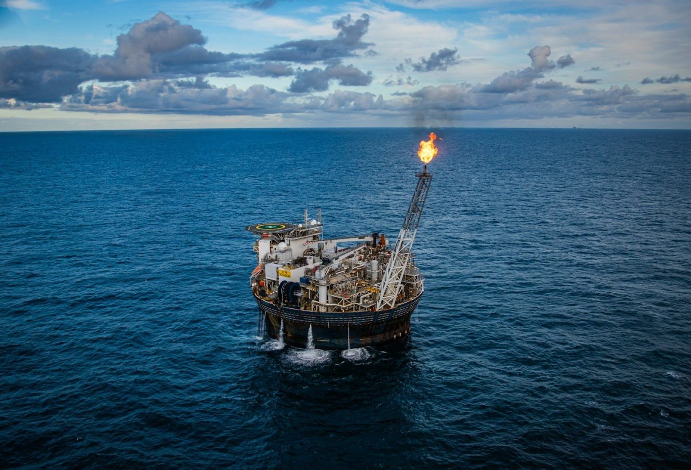 Offshore oil rig with a flare stack on a calm sea under a cloudy sky.