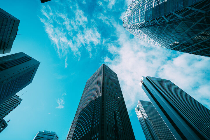 View of skyscrapers reaching towards a bright blue sky with scattered clouds.