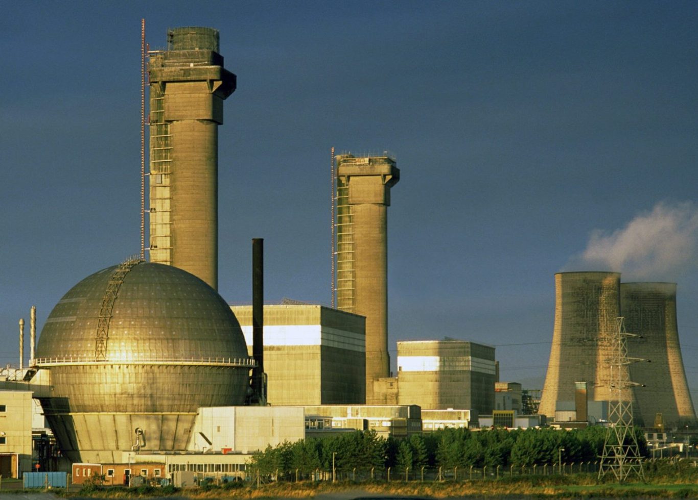 Power plant with large cooling towers, gas turbines, and a spherical storage tank.